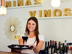 Das Bild zeigt Nina Kolok mit einer Flasche Wein auf einem Tablett.